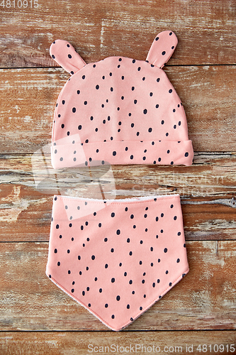 Image of pink baby hat with ears and bib on wooden table