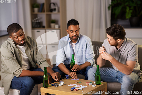 Image of happy male friends playing cards at home at night