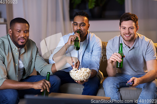 Image of happy male friends with beer watching tv at home