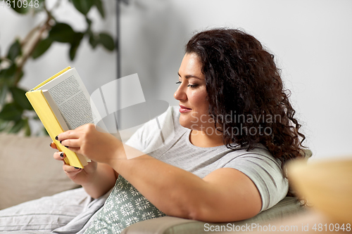 Image of young woman reading book on sofa at home