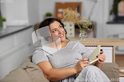 Image of happy young woman with diary on sofa at home