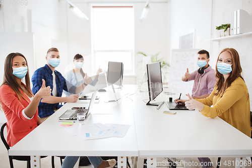 Image of business team in medical masks showing thumbs up