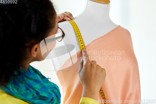 Image of fashion designer measuring dress with tape measure