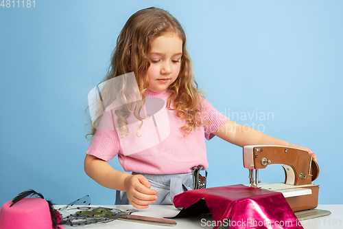 Image of Little girl dreaming about future profession of seamstress