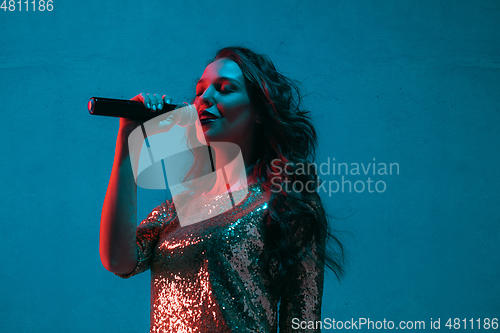 Image of Caucasian female singer portrait isolated on blue studio background in neon light