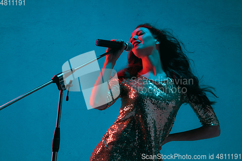 Image of Caucasian female singer portrait isolated on blue studio background in neon light