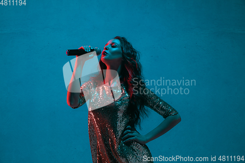 Image of Caucasian female singer portrait isolated on blue studio background in neon light