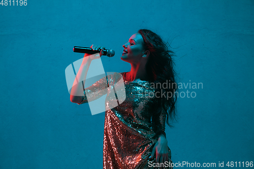 Image of Caucasian female singer portrait isolated on blue studio background in neon light