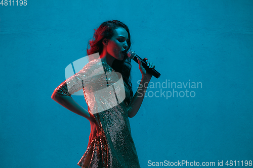 Image of Caucasian female singer portrait isolated on blue studio background in neon light