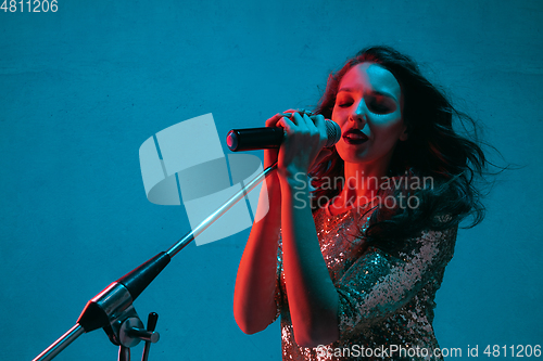 Image of Caucasian female singer portrait isolated on blue studio background in neon light