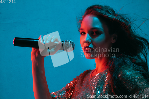 Image of Caucasian female singer portrait isolated on blue studio background in neon light