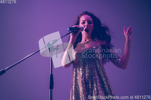 Image of Caucasian female singer portrait isolated on purple studio background in neon light