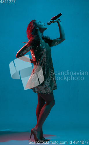 Image of Caucasian female singer portrait isolated on blue studio background in neon light