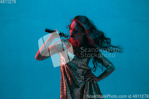 Image of Caucasian female singer portrait isolated on blue studio background in neon light