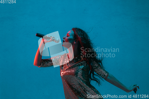 Image of Caucasian female singer portrait isolated on blue studio background in neon light