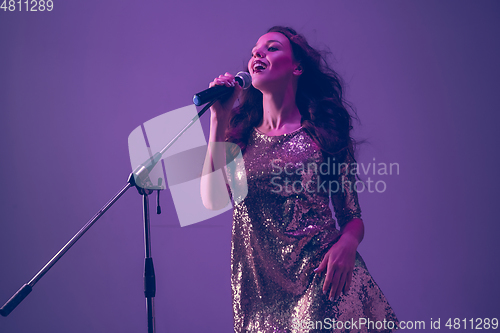 Image of Caucasian female singer portrait isolated on purple studio background in neon light