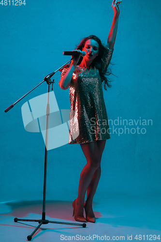 Image of Caucasian female singer portrait isolated on blue studio background in neon light