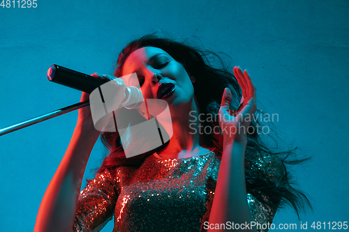 Image of Caucasian female singer portrait isolated on blue studio background in neon light