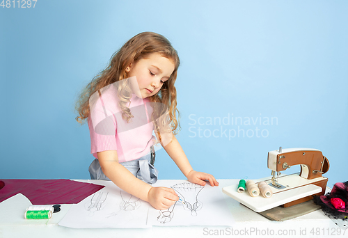 Image of Little girl dreaming about future profession of seamstress