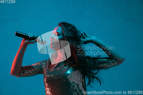 Image of Caucasian female singer portrait isolated on blue studio background in neon light