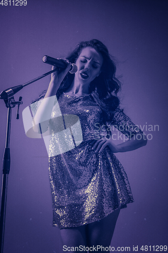 Image of Caucasian female singer portrait isolated on purple studio background in neon light