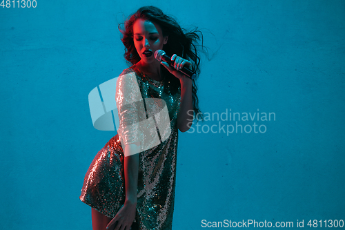 Image of Caucasian female singer portrait isolated on blue studio background in neon light