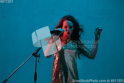 Image of Caucasian female singer portrait isolated on blue studio background in neon light