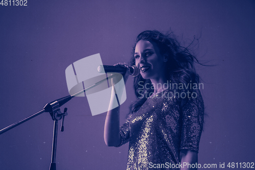 Image of Caucasian female singer portrait isolated on purple studio background in neon light