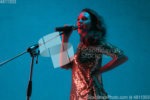 Image of Caucasian female singer portrait isolated on blue studio background in neon light