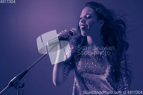 Image of Caucasian female singer portrait isolated on purple studio background in neon light