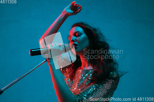 Image of Caucasian female singer portrait isolated on blue studio background in neon light