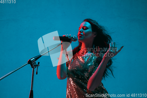 Image of Caucasian female singer portrait isolated on blue studio background in neon light