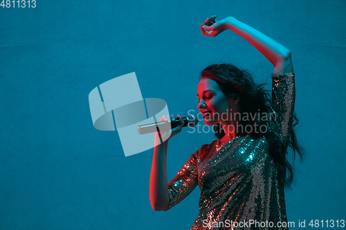 Image of Caucasian female singer portrait isolated on blue studio background in neon light