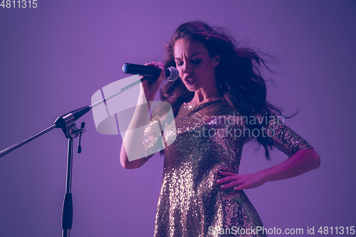 Image of Caucasian female singer portrait isolated on purple studio background in neon light