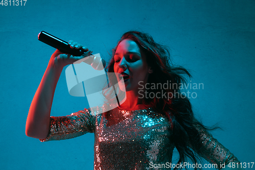 Image of Caucasian female singer portrait isolated on blue studio background in neon light