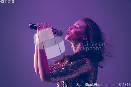 Image of Caucasian female singer portrait isolated on purple studio background in neon light