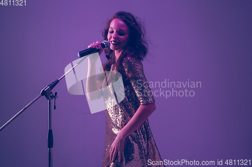 Image of Caucasian female singer portrait isolated on purple studio background in neon light