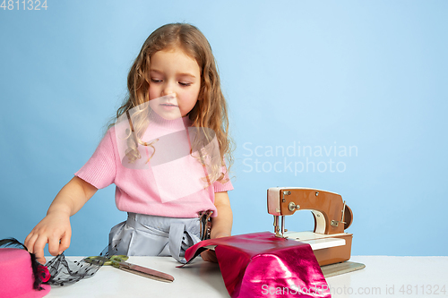 Image of Little girl dreaming about future profession of seamstress