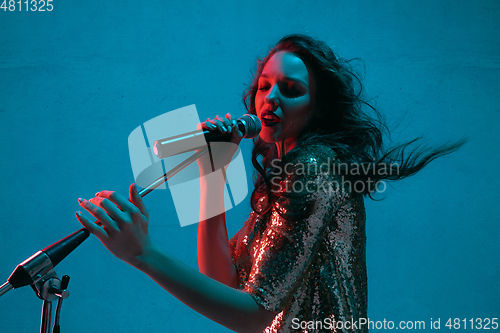 Image of Caucasian female singer portrait isolated on blue studio background in neon light