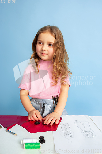 Image of Little girl dreaming about future profession of seamstress