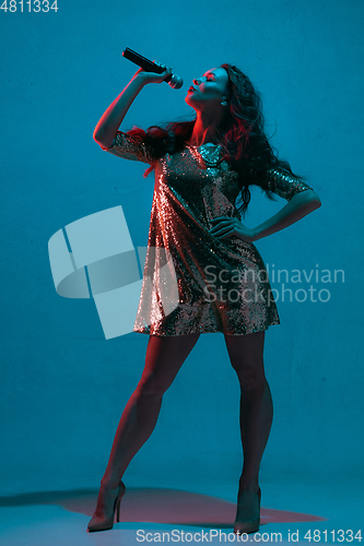 Image of Caucasian female singer portrait isolated on blue studio background in neon light