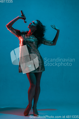 Image of Caucasian female singer portrait isolated on blue studio background in neon light