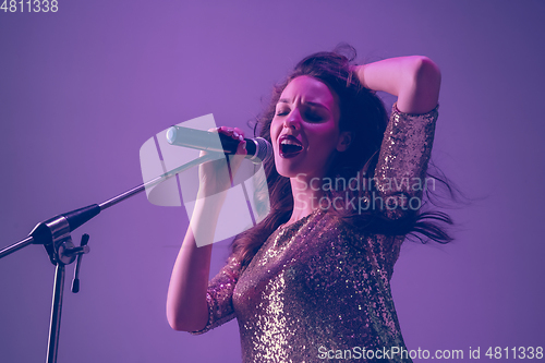 Image of Caucasian female singer portrait isolated on purple studio background in neon light