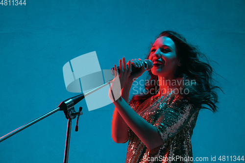 Image of Caucasian female singer portrait isolated on blue studio background in neon light