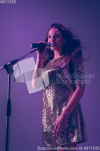 Image of Caucasian female singer portrait isolated on purple studio background in neon light