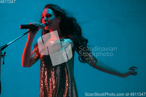 Image of Caucasian female singer portrait isolated on blue studio background in neon light