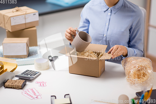 Image of woman packing mug to parcel box at post office