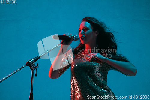 Image of Caucasian female singer portrait isolated on blue studio background in neon light