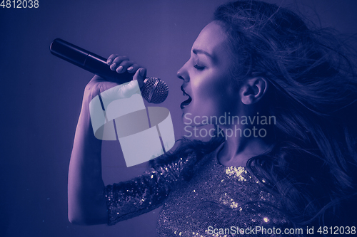 Image of Caucasian female singer portrait isolated on purple studio background in neon light