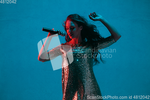 Image of Caucasian female singer portrait isolated on blue studio background in neon light